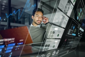 A man in a modern office setting interacts with a futuristic cloud-based surveillance interface. The semi-transparent digital display in front of him showcases security analytics, workplace security insights, and access control information, emphasizing secure office entry.