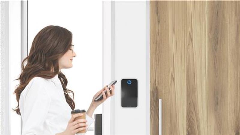 Woman uses a smartphone to unlock a secured door equipped with a wall-mounted access control system, representing modern cloud access control and seamless access control solutions in workplace environments.