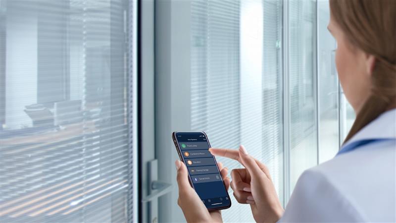 Professional woman navigating an access control app on her smartphone, demonstrating how cloud access control and visitor management systems allow flexible, secure access to various rooms within a modern office using integrated access control solutions.