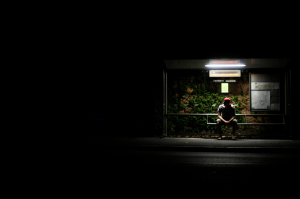 A person waiting at bus stop at night with obvious security risks.