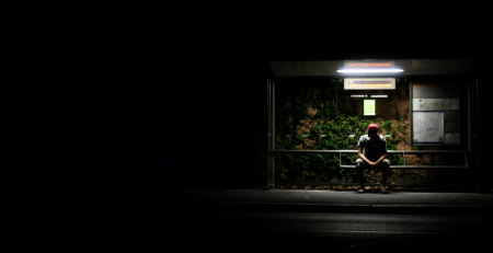 A person waiting at bus stop at night with obvious security risks.