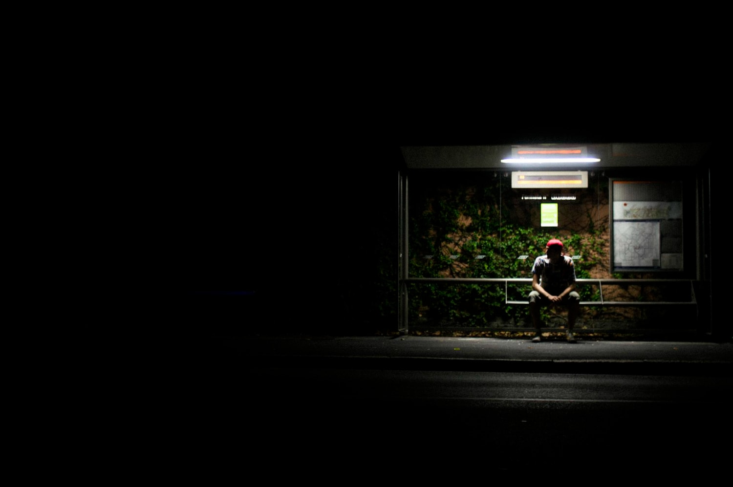 A person waiting at bus stop at night with obvious security risks.