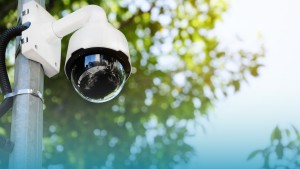 AI Virtual Security Guard Los Angeles concept showing a mounted outdoor surveillance camera monitoring a public area with trees in the background.